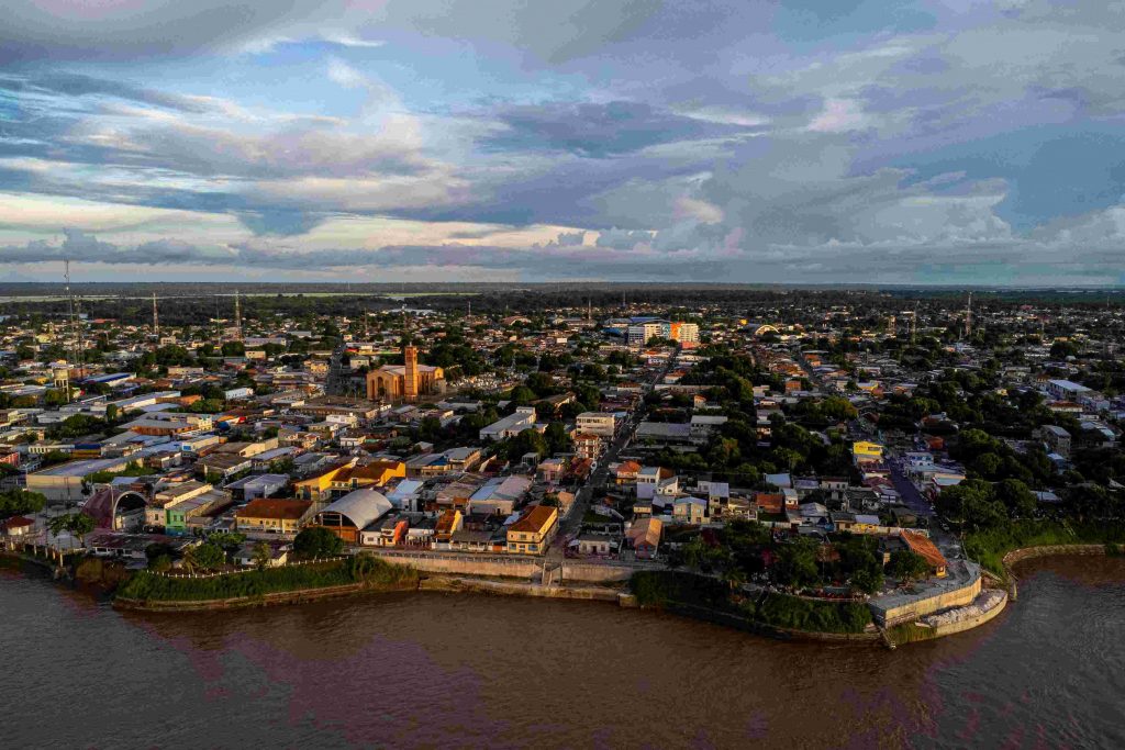 Visitantes passeiam de triciclo durante o Festival de Parintins 2024, com vista para o rio Amazonas