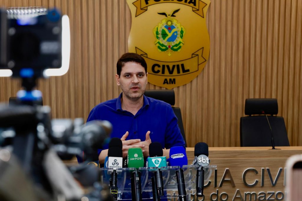 Um policial da Polícia Civil do Amazonas exibindo um telefone com os novos canais de denúncia: o número 197 e o número de WhatsApp.